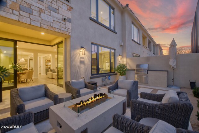 patio terrace at dusk featuring area for grilling, an outdoor living space with a fire pit, and an outdoor kitchen