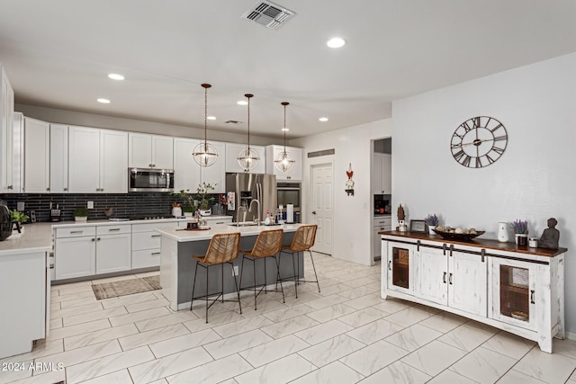 kitchen with decorative light fixtures, white cabinetry, stainless steel appliances, and an island with sink