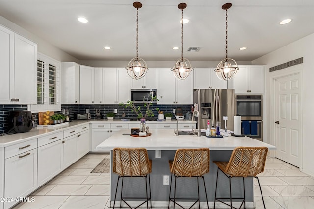 kitchen with backsplash, a kitchen island with sink, white cabinets, hanging light fixtures, and appliances with stainless steel finishes