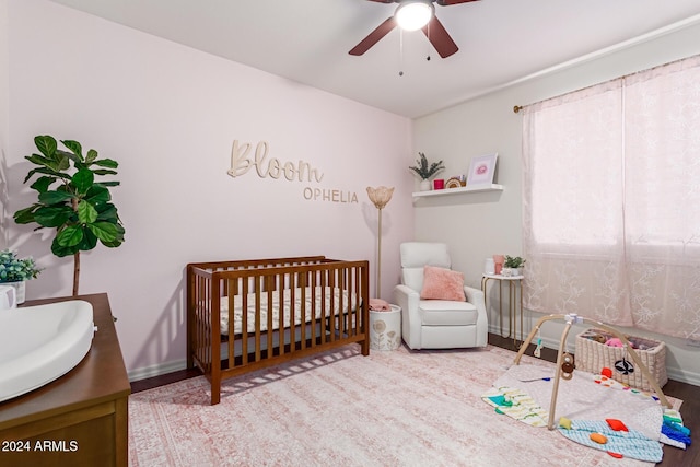 bedroom featuring a crib, wood-type flooring, ceiling fan, and sink