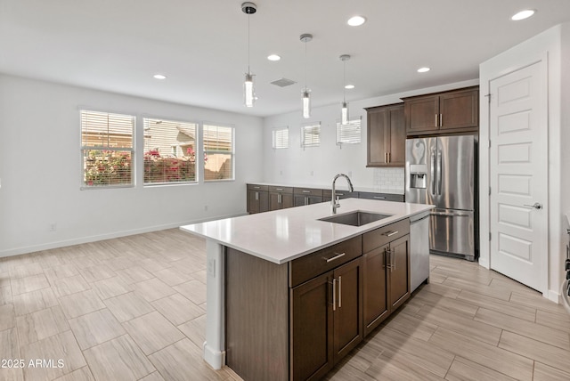 kitchen featuring stainless steel appliances, light countertops, dark brown cabinetry, a sink, and an island with sink