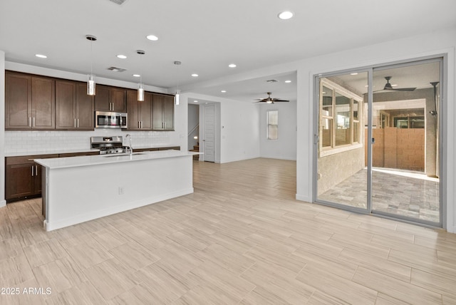 kitchen featuring light countertops, backsplash, appliances with stainless steel finishes, a kitchen island with sink, and dark brown cabinetry