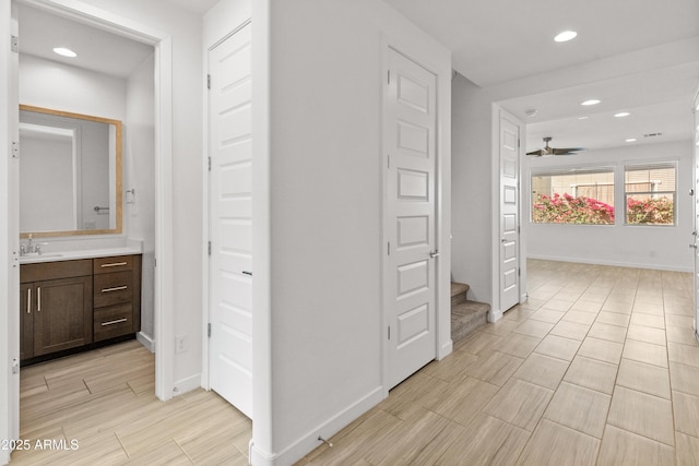 corridor featuring recessed lighting, wood finish floors, a sink, and baseboards