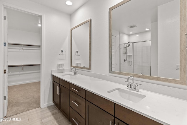 bathroom with double vanity, a spacious closet, a sink, and a shower stall