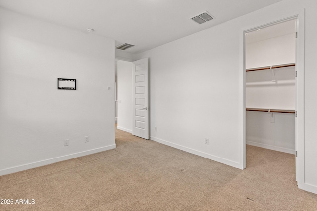 unfurnished bedroom with a spacious closet, carpet flooring, visible vents, and baseboards