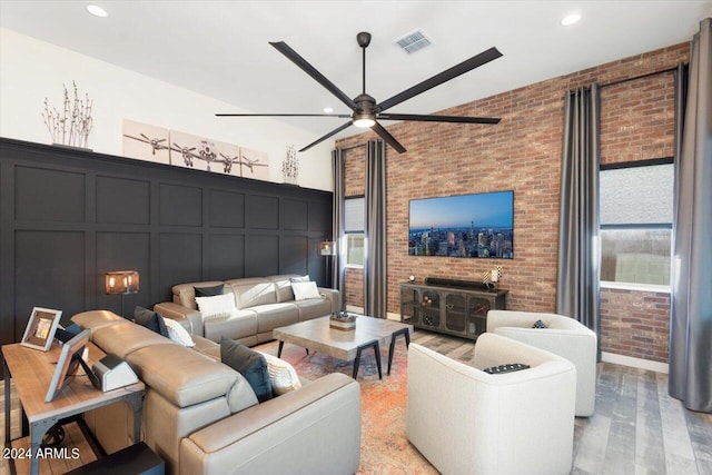 living room with ceiling fan, brick wall, and light wood-type flooring