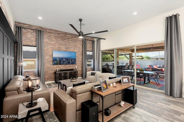 living room featuring ceiling fan, brick wall, a fireplace, and light hardwood / wood-style floors