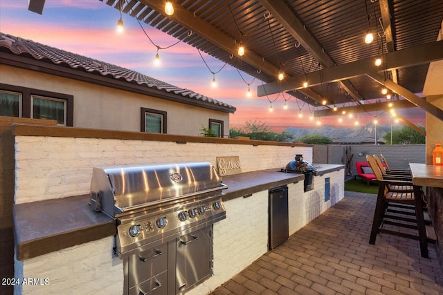 patio terrace at dusk with an outdoor kitchen, an outdoor bar, and area for grilling