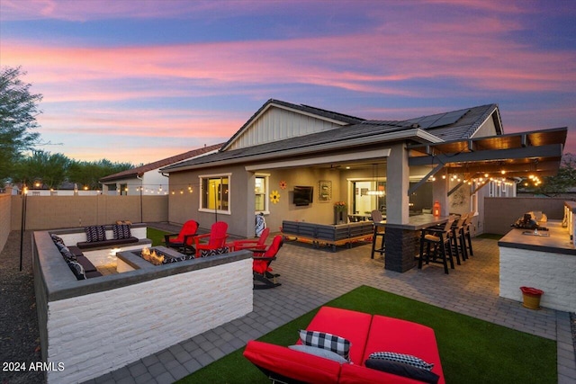 back of property featuring solar panels, exterior bar, an outdoor living space with a fire pit, and a patio area