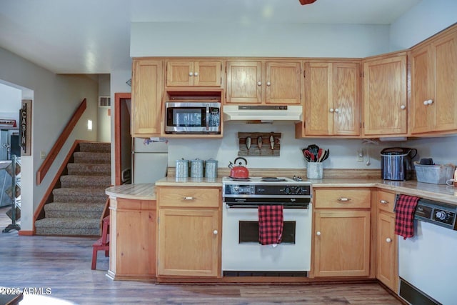 kitchen featuring white appliances, under cabinet range hood, light countertops, and wood finished floors