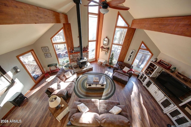 living room featuring baseboards, ceiling fan, wood finished floors, a wood stove, and high vaulted ceiling