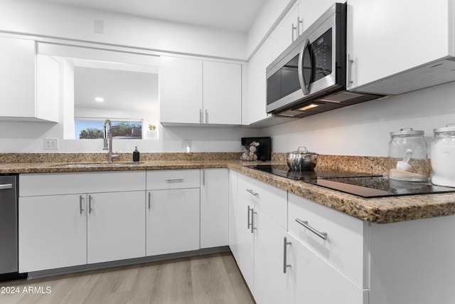 kitchen with sink, dark stone countertops, light wood-type flooring, appliances with stainless steel finishes, and white cabinetry