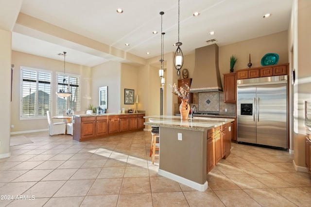 kitchen featuring a kitchen island with sink, appliances with stainless steel finishes, pendant lighting, and premium range hood