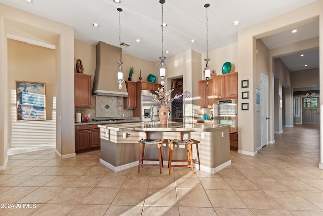 kitchen featuring light stone counters, appliances with stainless steel finishes, decorative light fixtures, a kitchen bar, and decorative backsplash