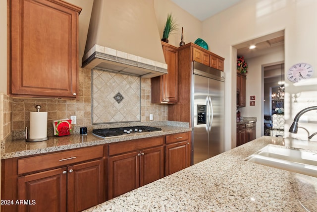 kitchen with premium range hood, light stone counters, stainless steel appliances, decorative backsplash, and sink