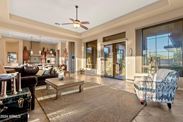 living room featuring ceiling fan, a tray ceiling, and light tile patterned flooring