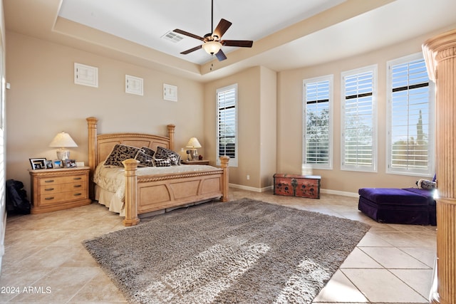 bedroom featuring a tray ceiling, multiple windows, light tile patterned floors, and ceiling fan