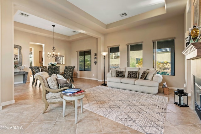 tiled living room with a tray ceiling, a chandelier, a tile fireplace, and plenty of natural light