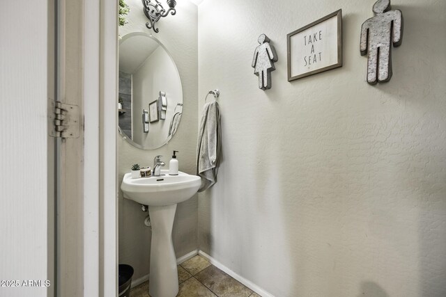 bathroom with tile patterned flooring, a textured wall, baseboards, and a sink