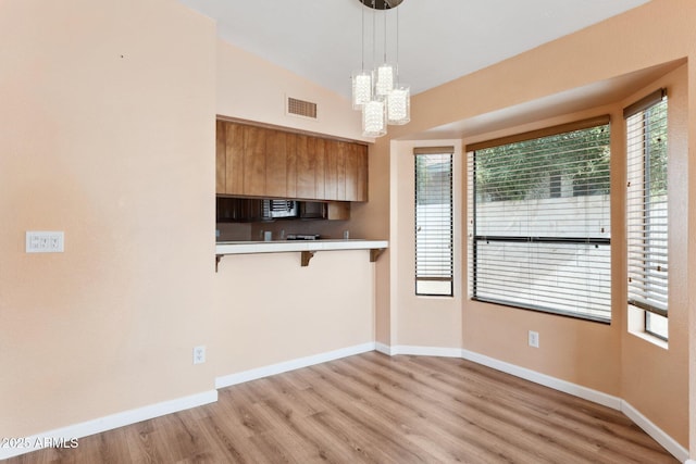 kitchen with a kitchen breakfast bar, hanging light fixtures, a notable chandelier, light hardwood / wood-style floors, and kitchen peninsula