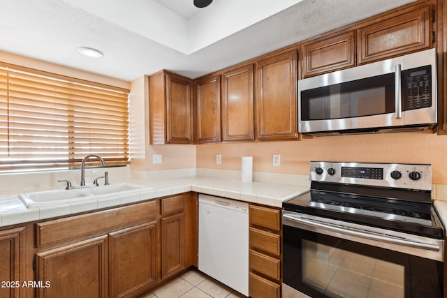 kitchen with stainless steel appliances, light tile patterned flooring, sink, and tile counters