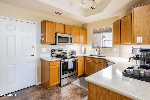 kitchen featuring a raised ceiling, dark tile patterned floors, appliances with stainless steel finishes, and sink