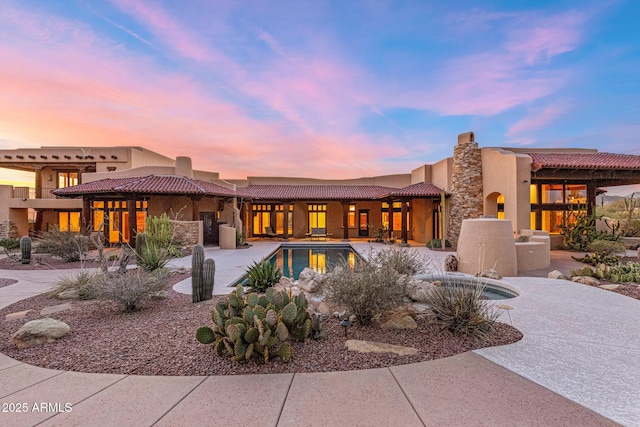 view of front of home with an outdoor pool, a patio area, curved driveway, and a tiled roof