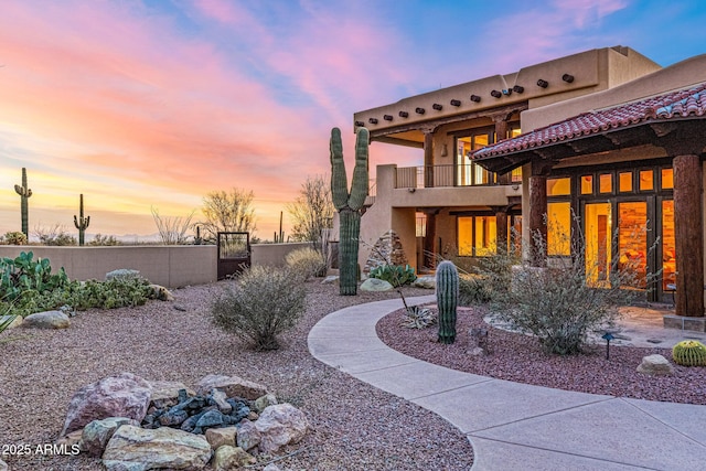 back of house at dusk featuring fence, a balcony, and stucco siding