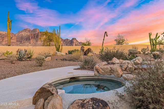 view of swimming pool with a mountain view, fence, and an in ground hot tub