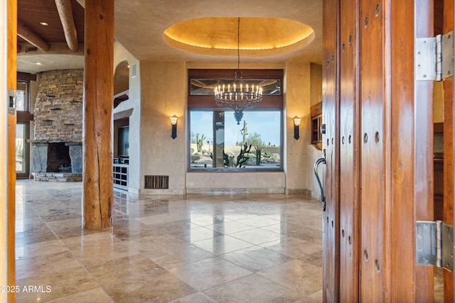 empty room featuring visible vents, a towering ceiling, a tray ceiling, a fireplace, and a chandelier