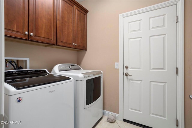 clothes washing area featuring cabinets, washing machine and clothes dryer, and light tile patterned floors