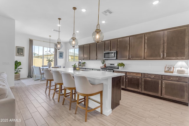 22634 E Roundup Way, Queen Creek, AZ 85142 - kitchen with appliances with stainless steel finishes, light countertops, dark brown cabinetry, a breakfast bar, and a center island with sink
