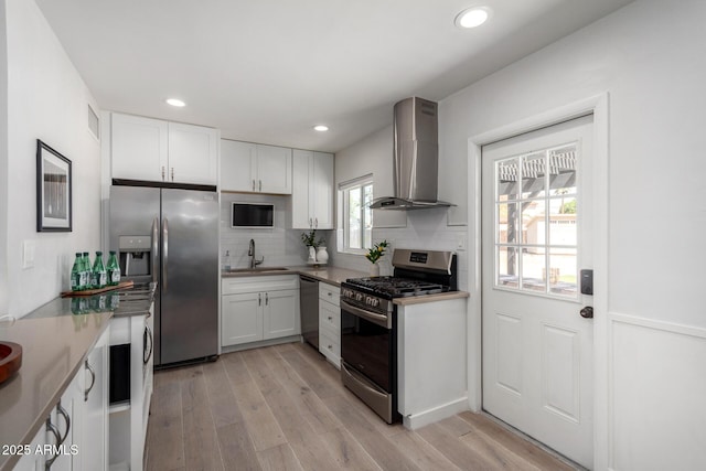 kitchen featuring appliances with stainless steel finishes, white cabinetry, wall chimney range hood, and a sink