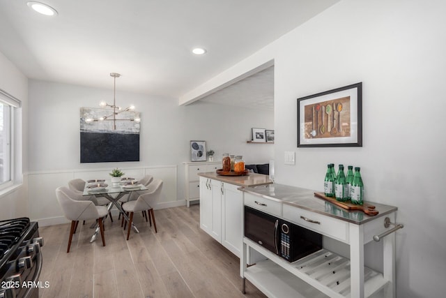 kitchen with light wood-style flooring, recessed lighting, stainless steel range with gas stovetop, white cabinets, and a chandelier