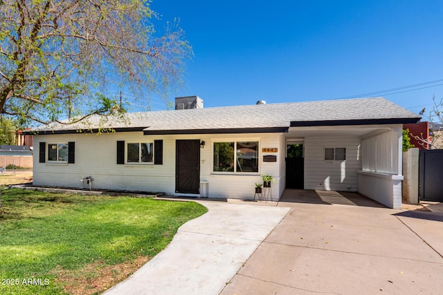 ranch-style home featuring driveway, an attached carport, roof with shingles, and a front yard