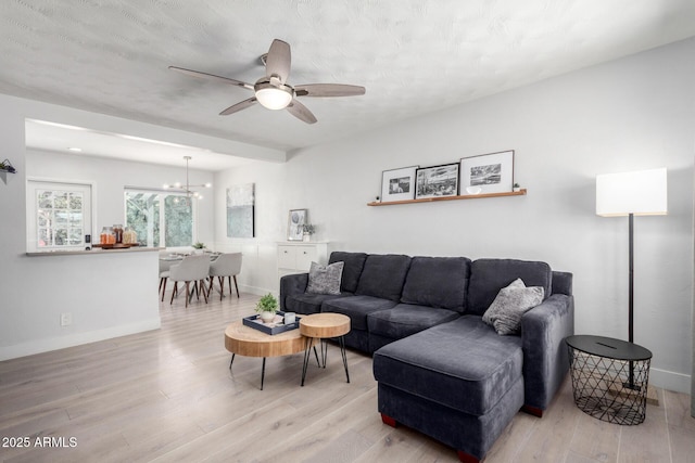 living area with ceiling fan with notable chandelier, wood finished floors, and baseboards