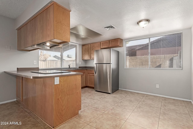 kitchen featuring light tile patterned floors, kitchen peninsula, a textured ceiling, and stainless steel refrigerator