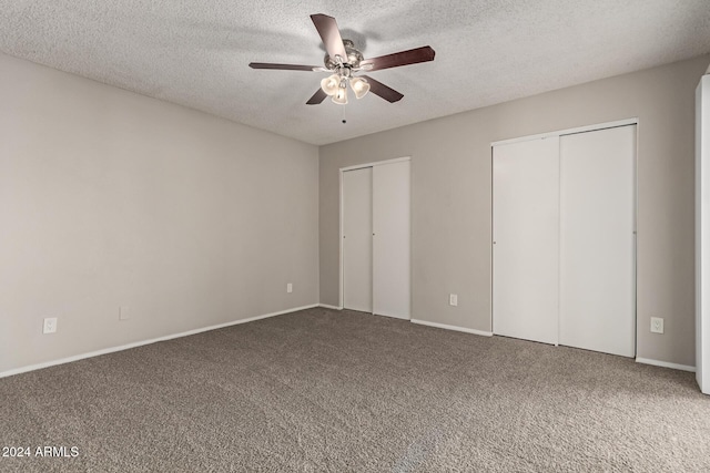 unfurnished bedroom featuring carpet flooring, a textured ceiling, two closets, and ceiling fan