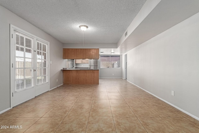 kitchen with kitchen peninsula, stainless steel fridge, plenty of natural light, and light tile patterned floors