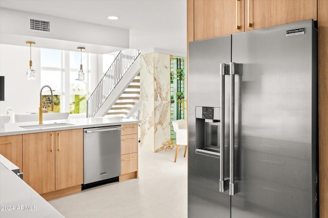 kitchen with decorative light fixtures, stainless steel appliances, light brown cabinetry, and sink