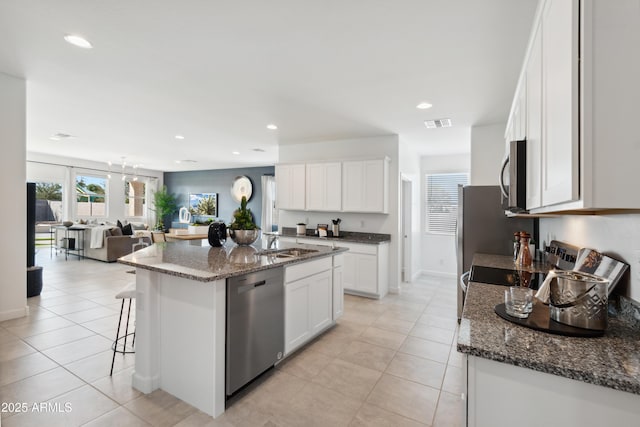 kitchen with light tile patterned flooring, white cabinetry, a center island with sink, dark stone countertops, and appliances with stainless steel finishes