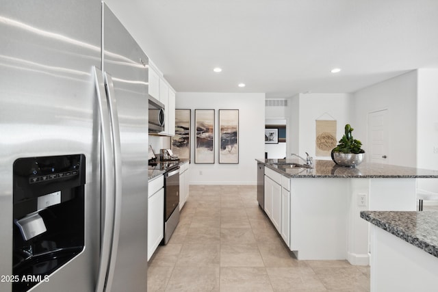 kitchen featuring appliances with stainless steel finishes, a kitchen island with sink, dark stone countertops, and white cabinets