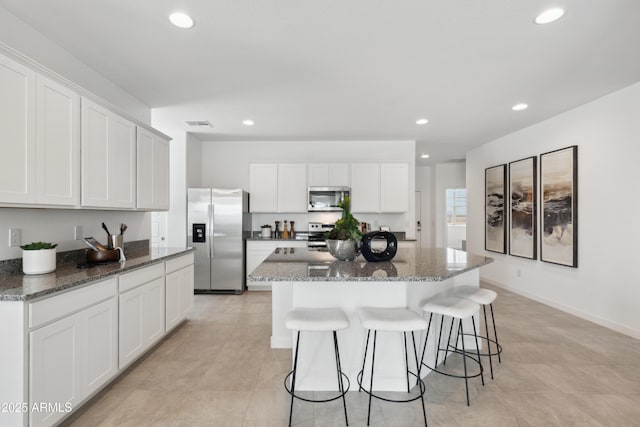 kitchen with white cabinetry, stainless steel appliances, a center island, and dark stone countertops