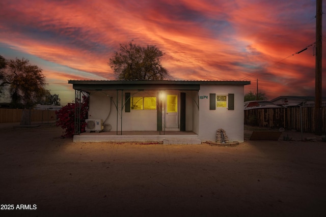 back of property at dusk featuring stucco siding, fence, ac unit, and covered porch
