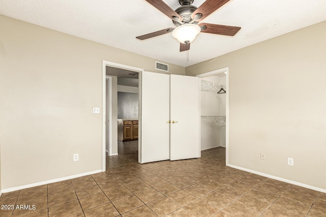 unfurnished bedroom with a textured ceiling, a walk in closet, tile patterned flooring, a closet, and ceiling fan