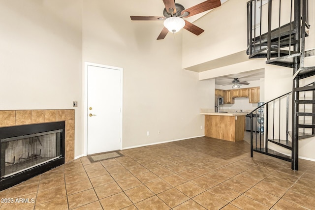 unfurnished living room featuring ceiling fan, a high ceiling, a fireplace, and tile patterned flooring