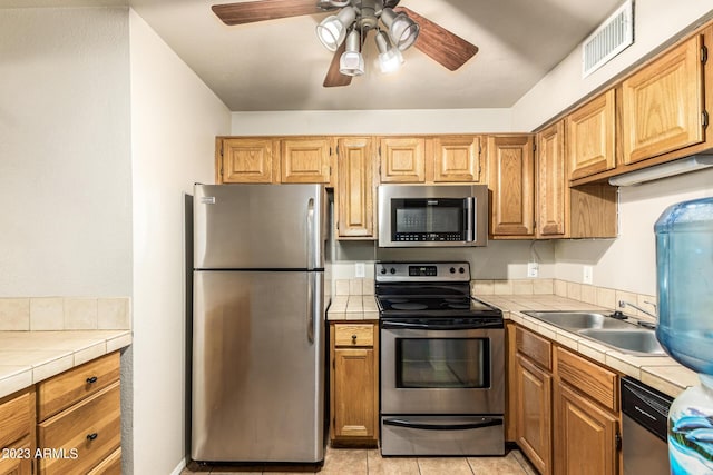 kitchen with sink, tile counters, light tile patterned floors, and stainless steel appliances