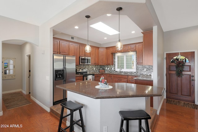 kitchen featuring a breakfast bar, a center island, decorative backsplash, appliances with stainless steel finishes, and dark hardwood / wood-style flooring