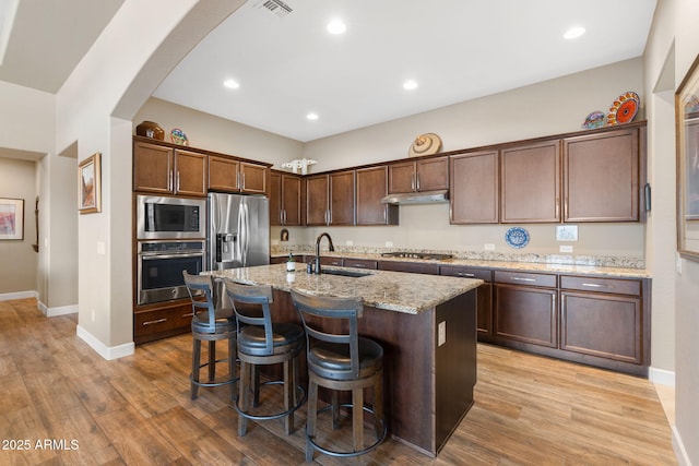 kitchen with sink, a center island with sink, light hardwood / wood-style flooring, appliances with stainless steel finishes, and light stone countertops