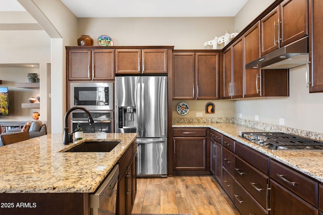 kitchen featuring sink, light hardwood / wood-style flooring, appliances with stainless steel finishes, light stone counters, and a center island with sink